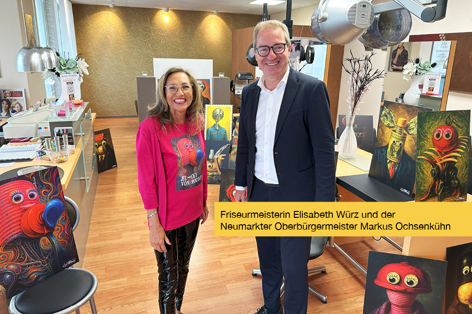 Friseurmeisterin Elisabeth Würz vom Haarstudio Elisabeth inmitten von einigen Kunstwerken des Künstlers Blacky von mococo, während der Bilderausstellung „exzellent unernst“ in Neumarkt.